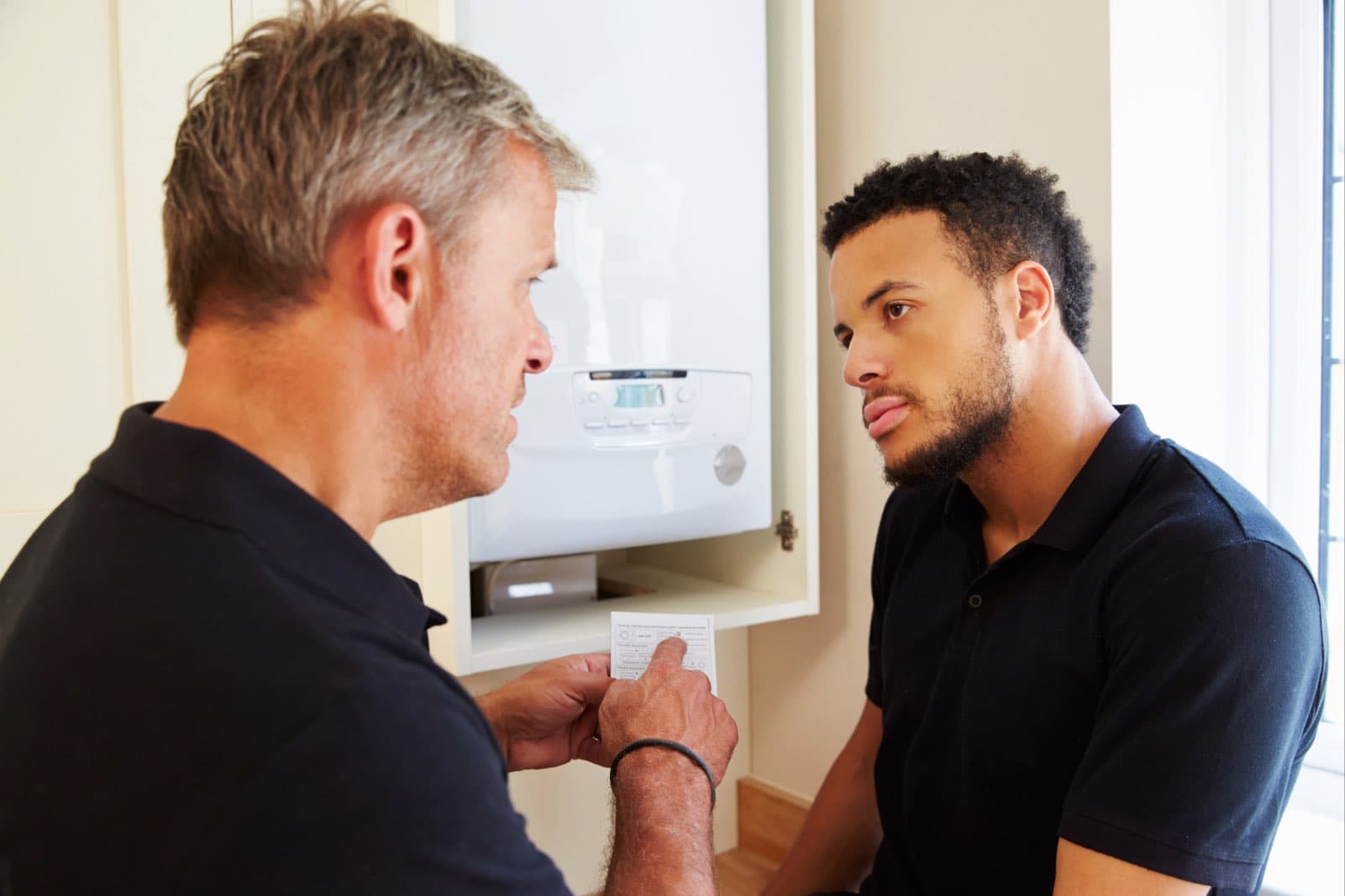 An engineer speaking with a customer beside a boiler.